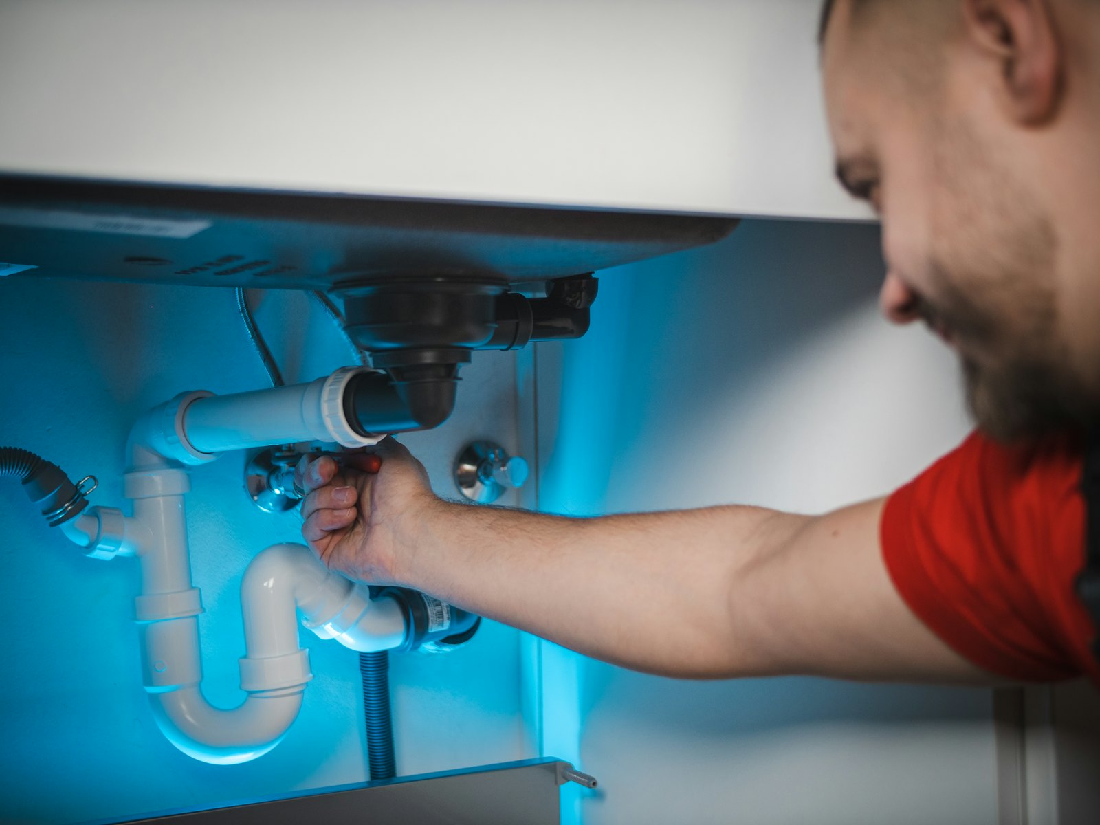 Plumber fitting the drain pipes under a sink